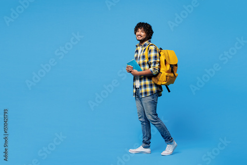 Konstfotografi Full body side view young smart Indian boy student wear yellow casual clothes backpack bag hold books looking camera walk go isolated on plain blue background
