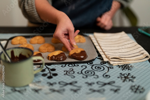 A person's hands dip heart-shaped cookies into melted chocolate on a baking sheet. They are preparing homemade sweets, a delicious treat for a special occasion or holiday. photo