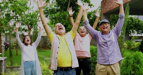 Seniors enjoying in laughter club outdoors, Indian Asian old age friends standing in lush green garden bursting in laughter with positive expressions in morning healthy activity
