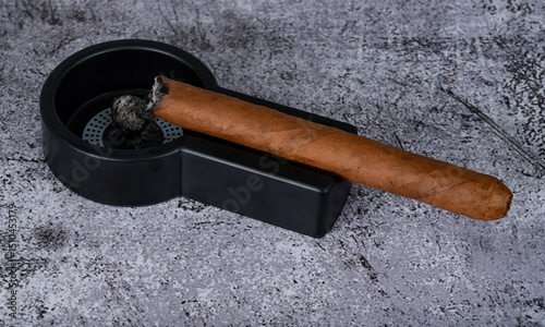 a lit cigar lies on an ashtray placed on the table
