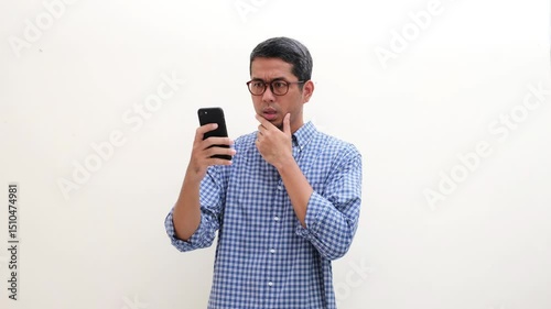 Adult Asian man showing shocked face expression after looking at his mobile phone