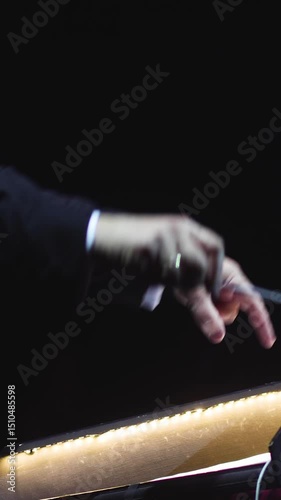 Male conductor behind the podium directing orchestra on stage with pupitre, musicians and choir, the philharmonic venue hall during concert, symphony orchestra director hands conducting waving baton