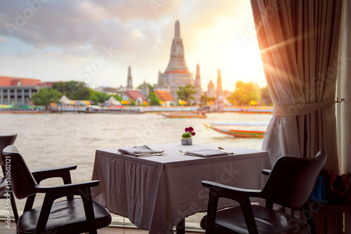 Photography Elegant riverside table set for two, overlooking Wat Arun temple at golden hour—