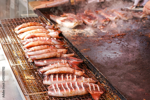 Juicy whole squids are neatly lined up on a searing iron plate, slowly caramelizing with spice, filling the air with a mouthwatering smoky scent.