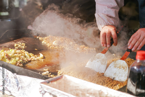 A chef’s hands skillfully work two spatulas, blending ingredients on the hot surface, creating a delicious street food favorite.