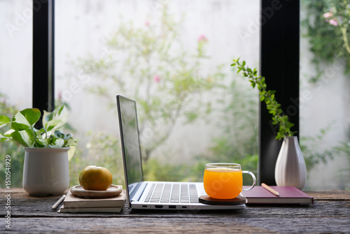 Side view of a laptop with orange juice, and potted plants on rustic desk
