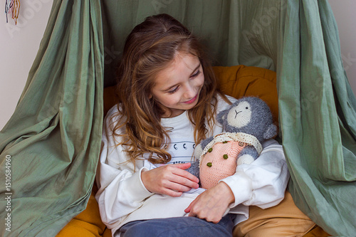 Beautiful little girl in comfortable clothes sits in children's room interior with knitted toy kigurumi in hands, selective focus	