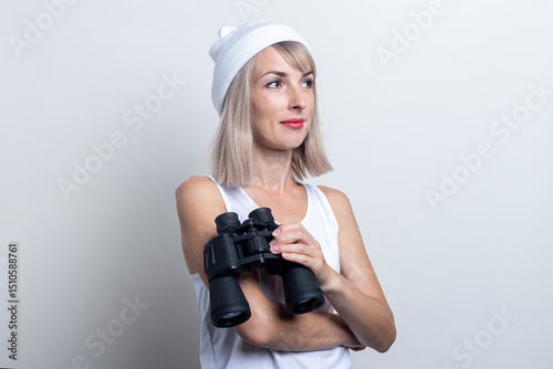 Young woman holding binoculars looks to the side on a light background