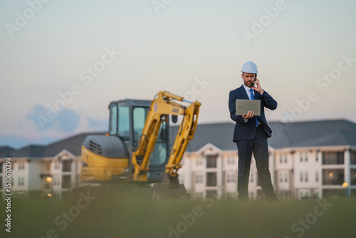 Construction manager in suit and helmet at a construction site. Construction manager worker or supervisor wearing hardhat in front of house. Supervisor construction manager near excavator. Renovation.