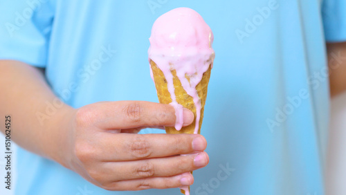 Child holding melting pink strawberry ice cream cone, sticky drips cascading down waffle cone against bright blue background