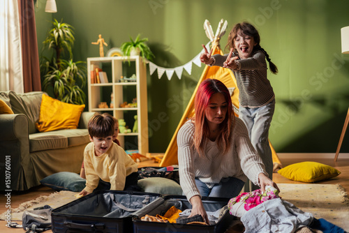 Mother packing suitcase with playful children in living room