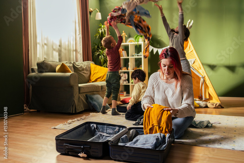 Mother packing suitcase while children playing at home