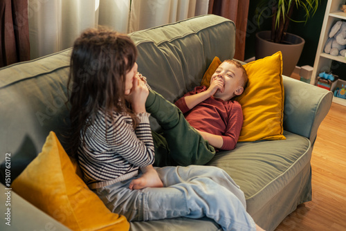Girl tickling her brother's feet on sofa, making him laugh