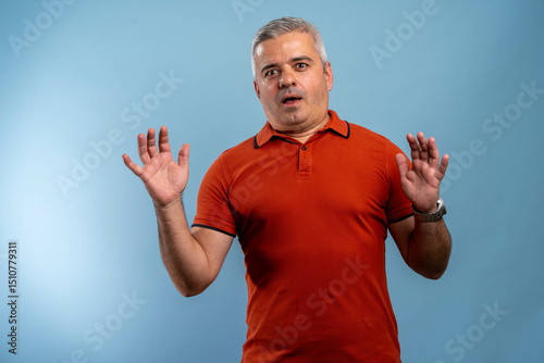 Frightened mature man with worried expression standing against blue background. Emotional reaction, stress, fear, and panic concept.