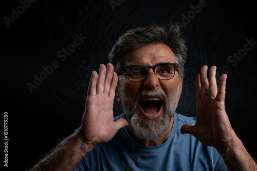 Handsome mature bearded man, very cheerful and enthusiastic, announcing information with his hands cupped around his mouth. Dark background highlights his positive energy.