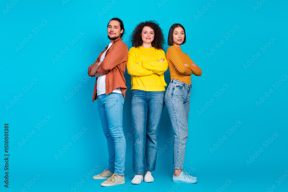 Fototapeta premium Three diverse young friends confidently pose together in casual outfits against a vibrant blue background, embodying unity and friendship