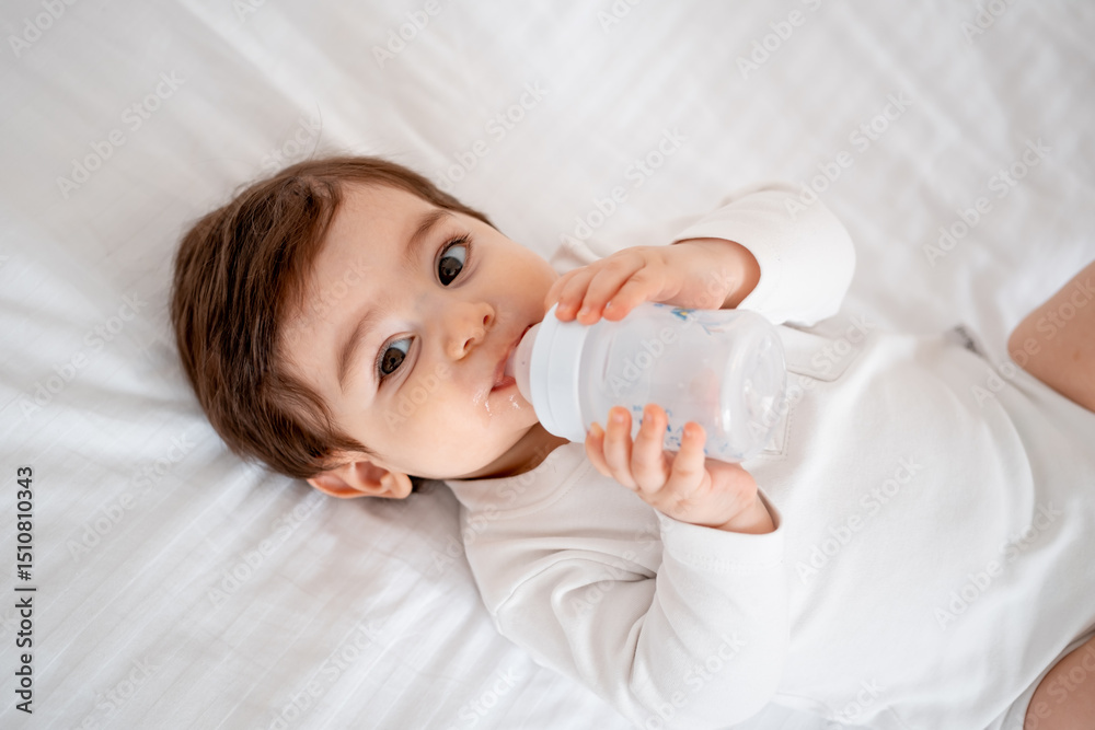 baby with a bottle of milk or water on a white bed at home, baby food feeding concept, place for text, cute smiling little baby baby with a bottle of milk or water on a white bed at home, baby food feeding concept, place for text, cute smiling little baby