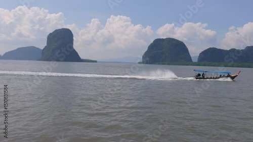 A picturesque scene of limestone formations with a boat's wake cutting through the calm water under a clear sky in Phuket.