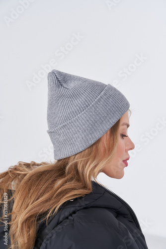 Fashionable woman in stylish gray beanie and jacket poses against simple backdrop