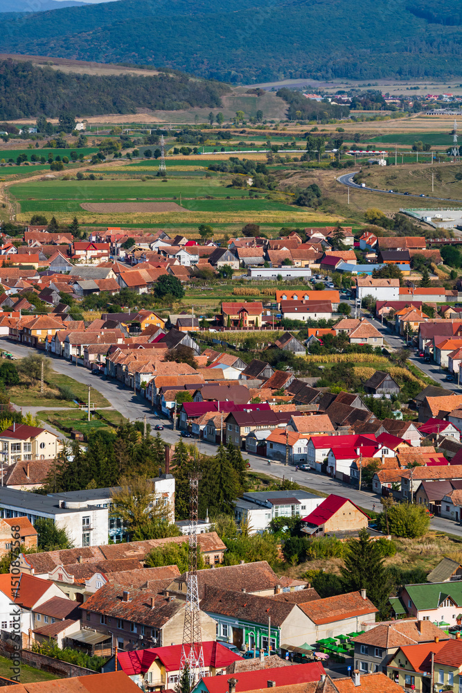 Obraz premium Aerial view of the town center with hills, buildings, streets, vegetation and surroundings in Rupea, Romania, 2021