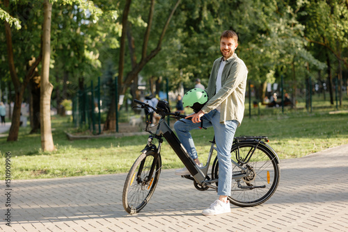 Young man enjoys cycling in a green park on a sunny day while wearing a helmet and smiling