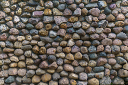 Wall fence of stones of different sizes roughly stacked on top of each other and fastened with cement. Construction industrial background.