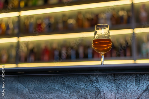 Whiskey glass close-up on bar counter with blurred background of shelves with alcoholic drinks photo