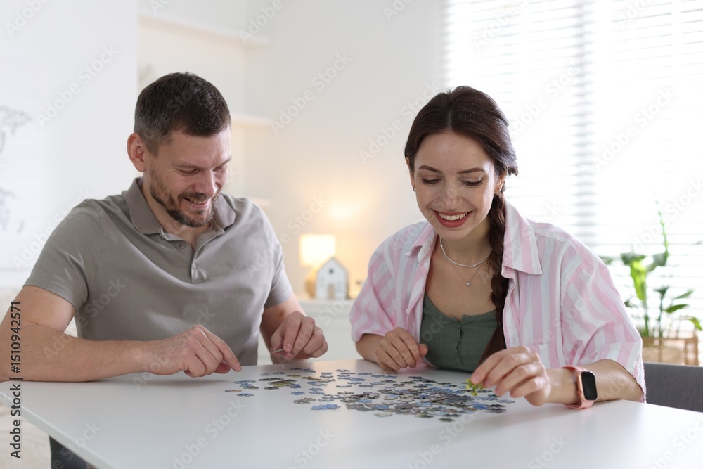Happy couple solving puzzle together at white table indoors Happy couple solving puzzle together at white table indoors