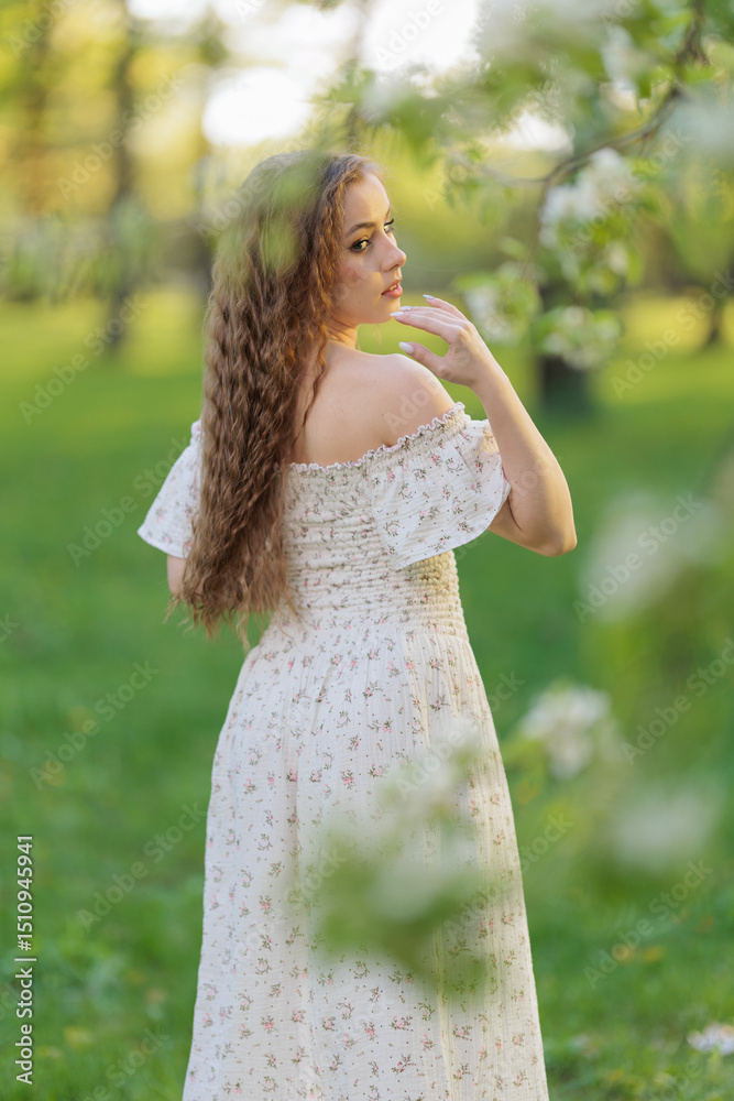 Beautiful Girl with long hair in a white dress poses near white blossoming apple trees Beautiful Girl with long hair in a white dress poses near white blossoming apple trees