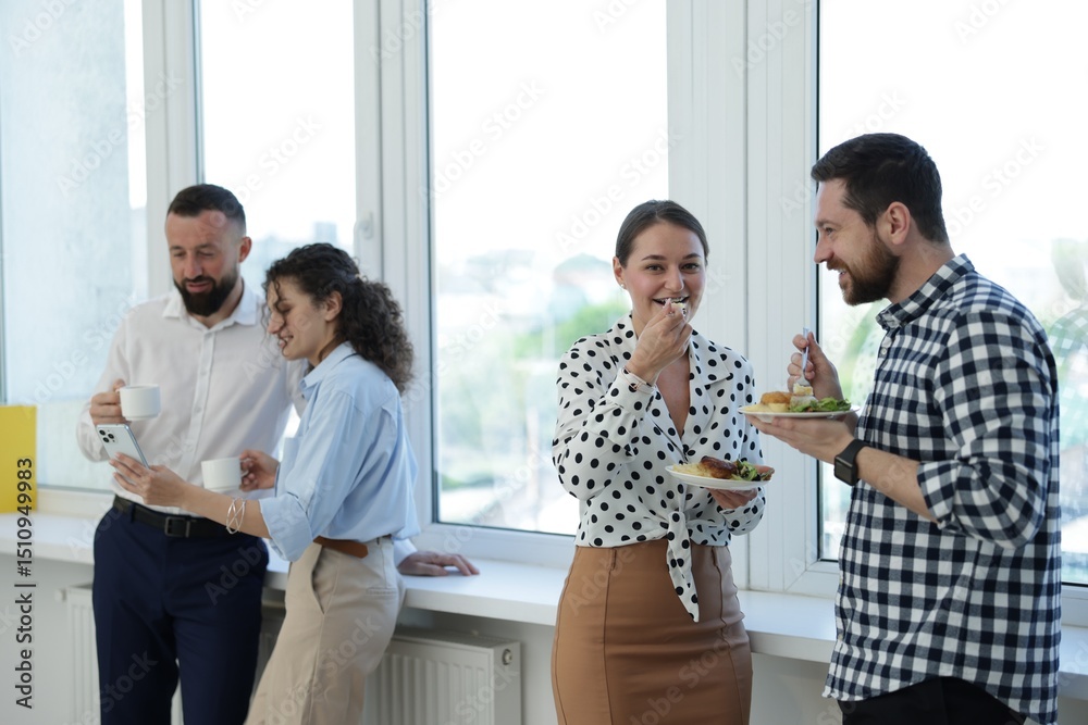 Obraz premium Colleagues with food and drinks near window in office during lunch break