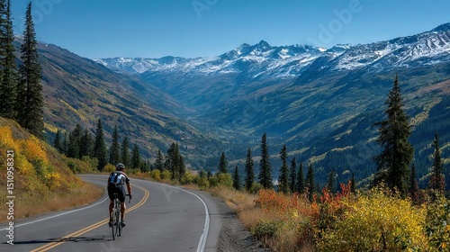   A man rides a bike down a winding road in front of snow-capped mountain peaks