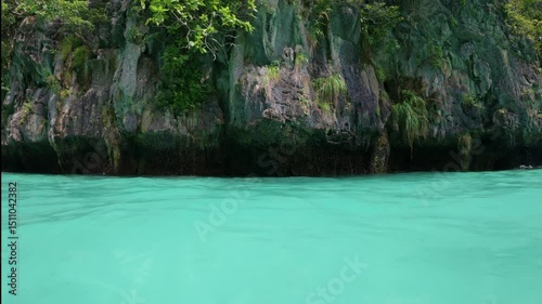 Boats glide through turquoise waters, surrounded by green cliffs in Phuket, Thailand.
