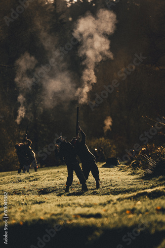 A vertical photograph of Silhouettes of guns shooting with gun smoke on a pheasant shoot in UK