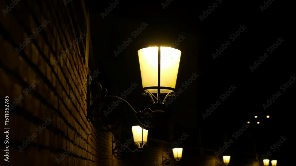 Vintage street light on a brick wall is illuminating the night. The light creates a warm glow, contrasting with the darkness surrounding it