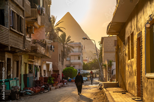 View of Giza Pyramid and local woman in Cairo backstreet during golden hour, Cairo, Egypt, Africa