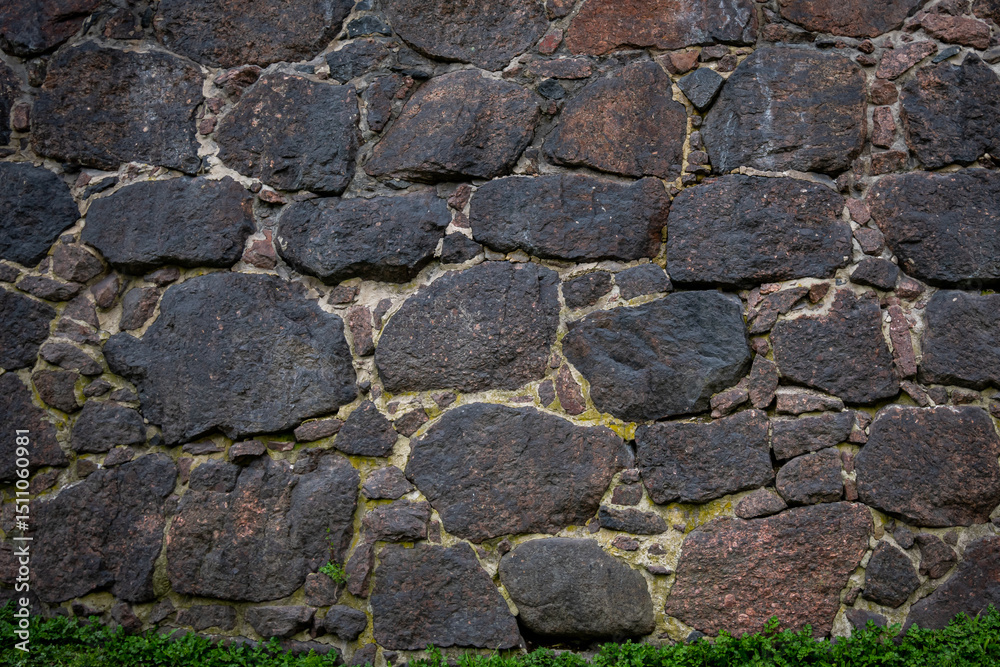 Obraz premium A wall of large granite stones with a green strip of grass growing at the bottom