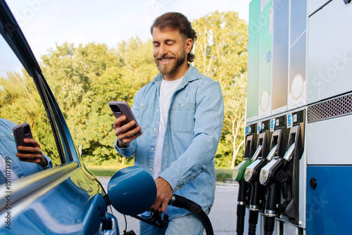 Canvastavla Happy man driver filling his car with fuel at the gas station and using cellphon