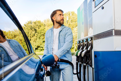 Fotografie Handsome bearded European man refueling his car and looking on scoreboard, stand