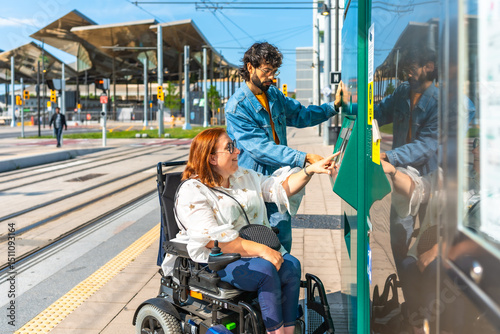 Woman in wheelchair and friend buying tram ticket at station