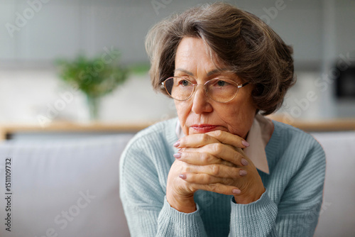 Thoughtful sad elderly woman sitting on couch, pensive older female looking into distance, thinking about problems