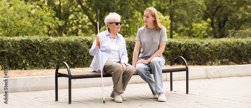 Young woman with blind grandmother sitting on bench in park