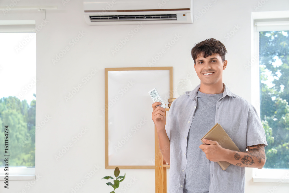 Fototapeta premium Young man with book turning on air conditioner at home