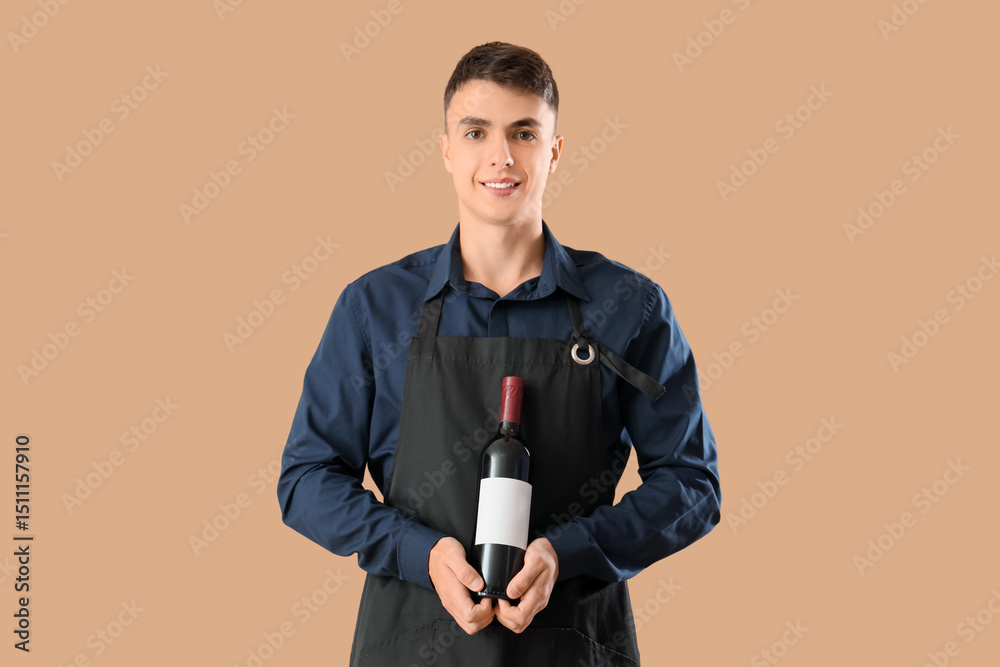 Naklejka premium Young male waiter with bottle of wine on beige background
