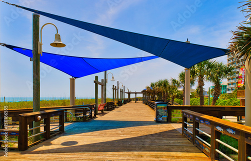 Φωτογραφία A view down a wooden beach boardwalk with shade tarps and their shadows at Carolina Beach, North Carolina USA