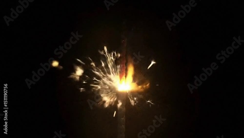 A lit sparkler emits bright sparks and trails of smoke against a completely black background.
