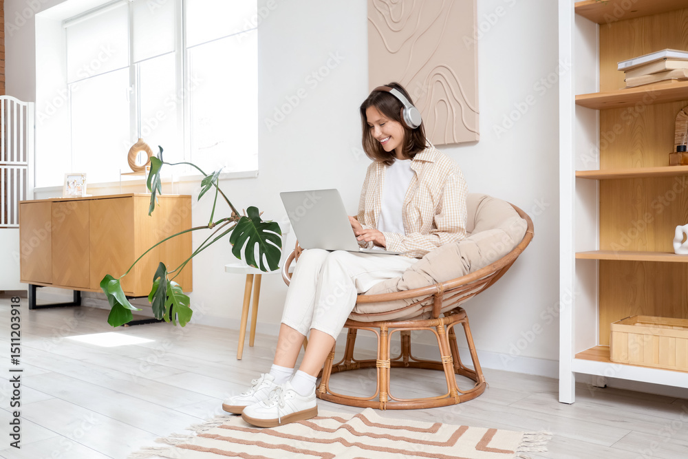 Young woman with headphones using laptop in cocoon chair at home Young woman with headphones using laptop in cocoon chair at home