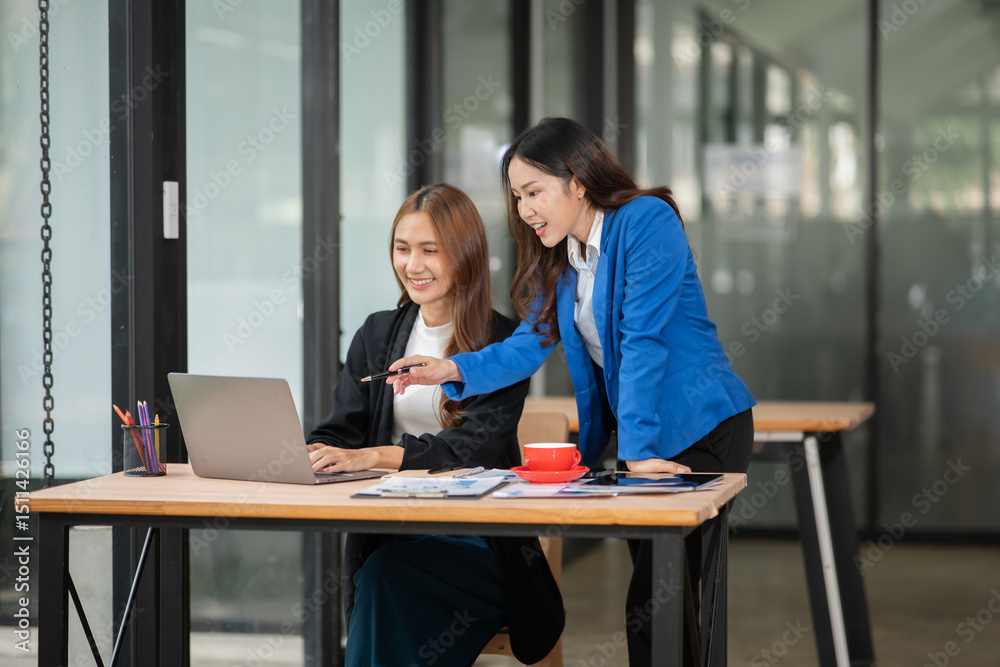 Fototapeta premium Two Asian businesswomen using laptops, on the table there are graph documents working on business investment.