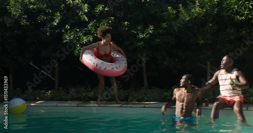 Diverse friends laughing and splashing in pool with colorful inflatables on sunny day