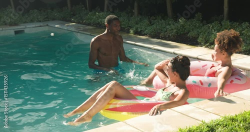 Diverse friends enjoying pool time, laughing and relaxing on floaties in sunny backyard