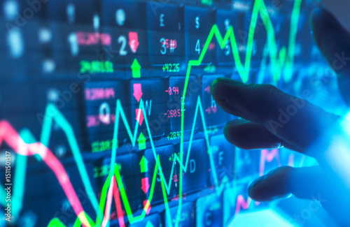 Hand interacting with financial data on a digital screen showing stock market graphs photo